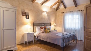 Un dormitorio con cama, mesitas de noche, armario y ventana con cortinas.