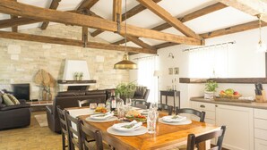 Un comedor con una mesa de madera dispuesta para una comida, rodeada de sillas, con una pared de piedra y una chimenea al fondo.