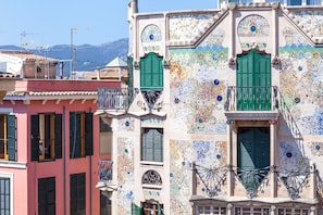 A building with colorful mosaic tiles, green shutters, and balconies with wrought iron railings.