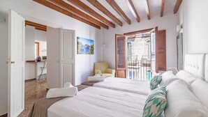 A hotel room with two beds, wooden beams on the ceiling, a chair, a painting, and a view through a door.