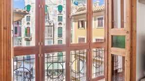 A view through a wooden-framed window with multiple panes, revealing a street with colorful buildings and balconies.