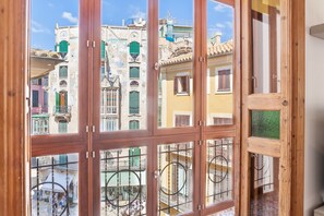 A view through a wooden-framed window with multiple panes, revealing a street with colorful buildings and balconies.