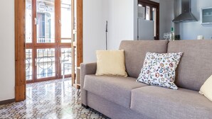 A living room with a sofa, two pillows, a floor lamp, and a view of a balcony with a railing.