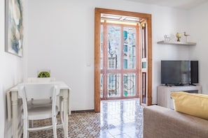 Un salon comprenant un téléviseur, un canapé, une table à manger avec une chaise, et une vue sur l’extérieur à travers une porte vitrée.