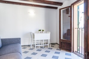 Une pièce avec un canapé blanc, une petite table blanche et deux chaises, et une porte en bois donnant sur un espace extérieur.