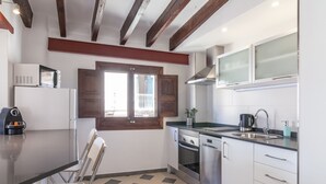 Una cocina compacta con microondas, horno y lavaplatos, vigas de madera en el techo y una ventana con contraventanas.