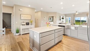 A modern kitchen with a central island, white cabinetry, and a view of the outdoors. - Stylish 4BR Majestic Retreat • Stunning Views of Table Rock Lake! (Branson)