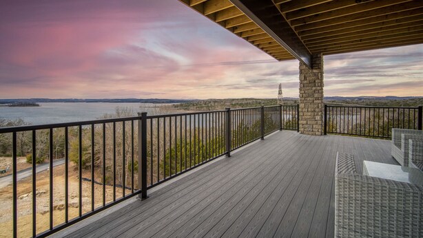 A wooden deck with a stone pillar, overlooking a body of water and distant hills. - Stylish 4BR Majestic Retreat • Stunning Views of Table Rock Lake! (Branson)