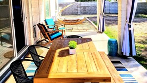 An outdoor patio with a wooden table, chairs, and a hanging plant.