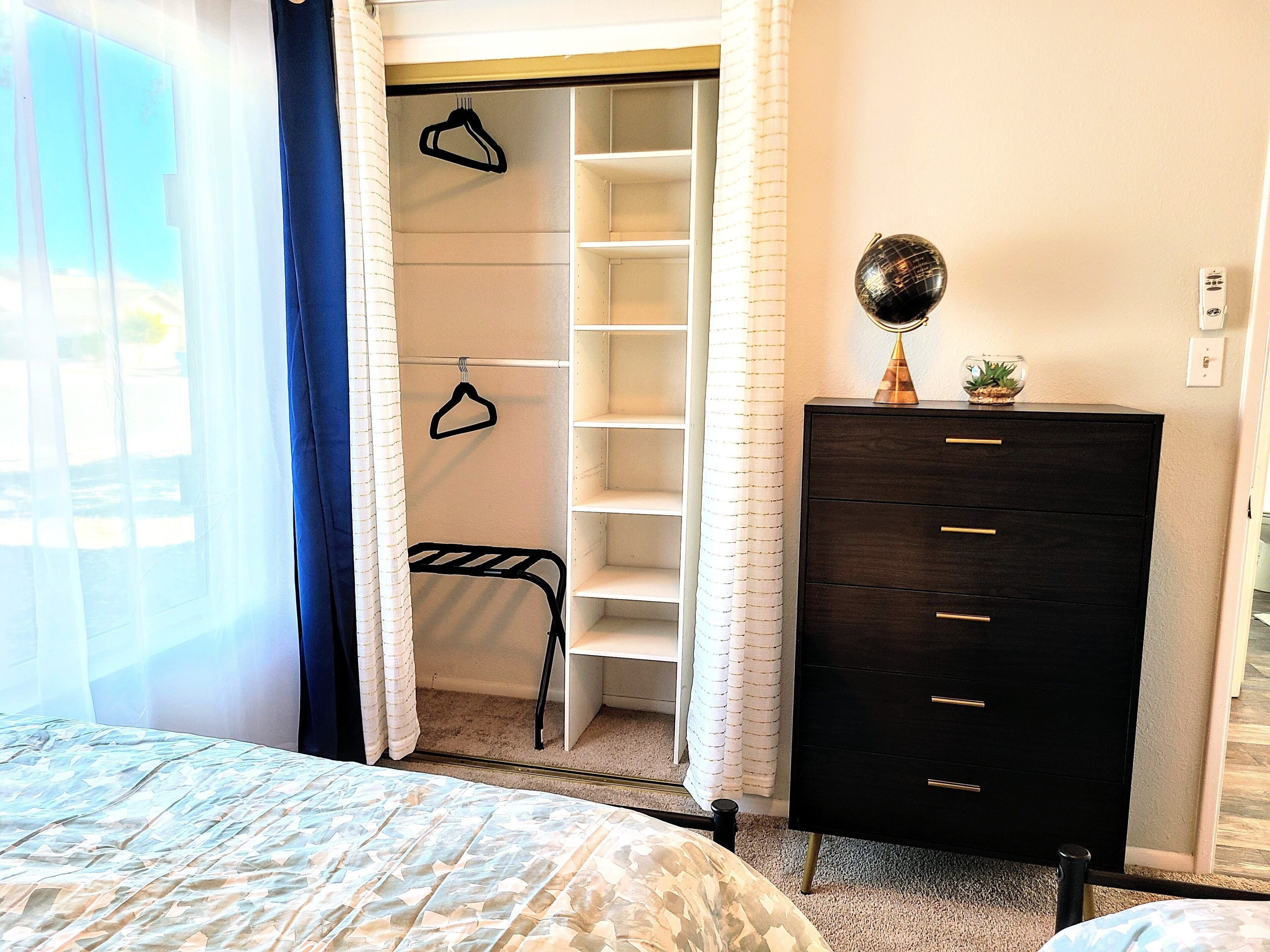 A bedroom with a bed, a wardrobe, a hanging rack, and a small table with a globe and plant.