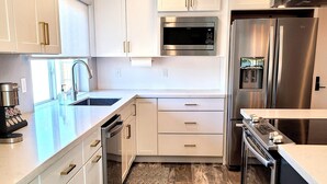 A modern kitchen with white cabinetry, stainless steel appliances, and a wooden floor.