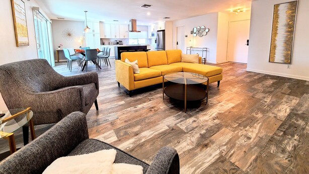 A spacious living room with a yellow sectional sofa, a grey armchair, and a glass coffee table.