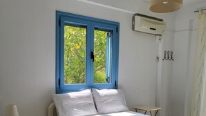 A bedroom with a bed, a nightstand, a window with blue shutters, and a hanging light fixture. - Villa Rahes,sea view,3 bedrooms,wifi,5min from the village,low prices (skopelos)