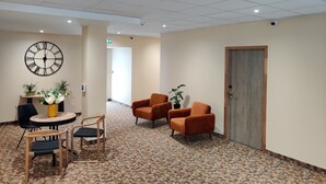 A lobby with a clock, seating area, and a door. - Hôtel de la Tour (La Tour-du-Pin)