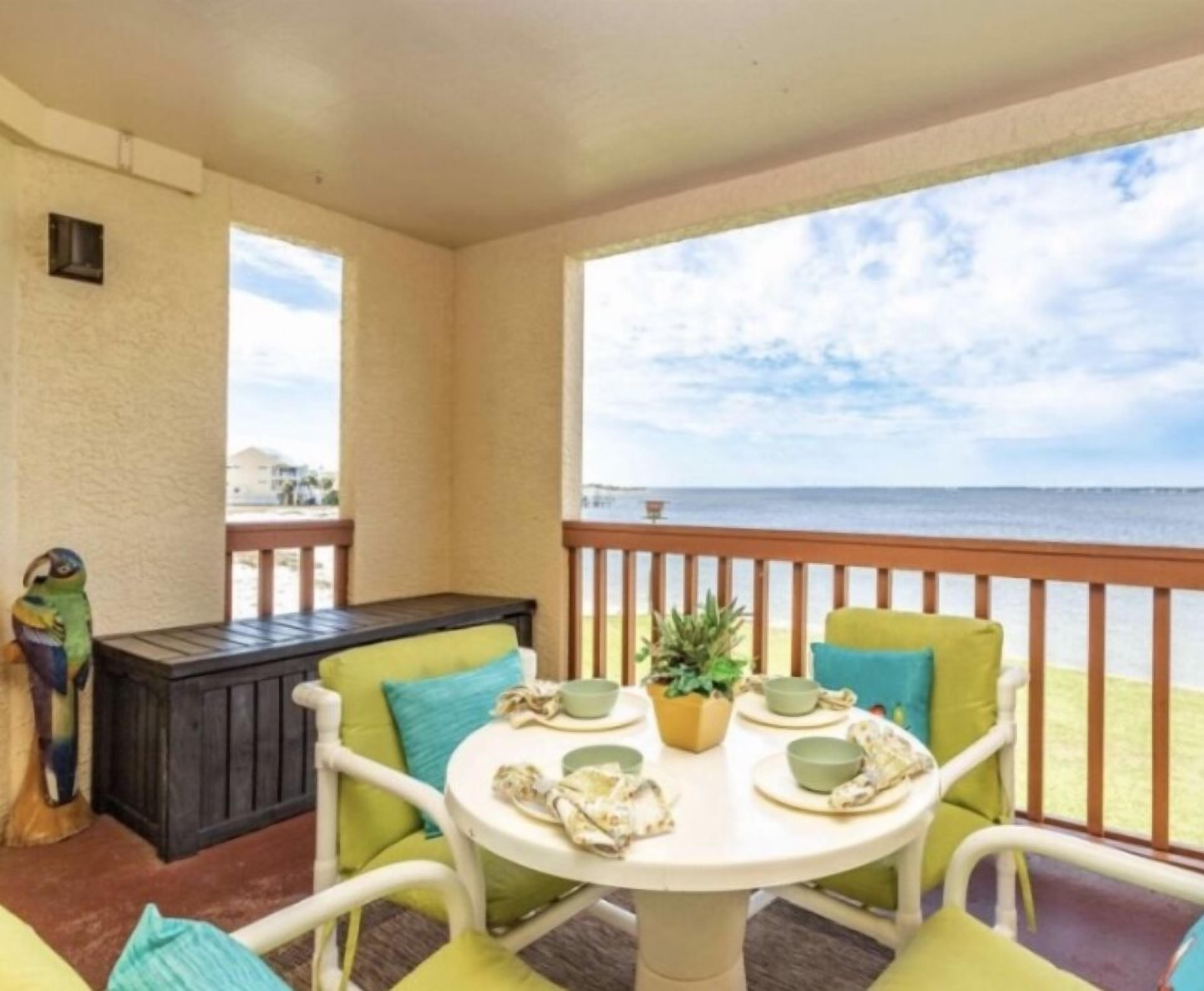 A balcony with a table set for two, chairs, a small plant, and a view of the ocean.