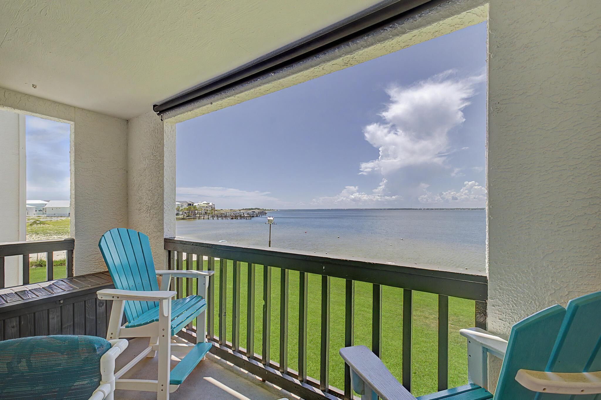 A balcony with a view of the sea, a pier, and a grassy area.