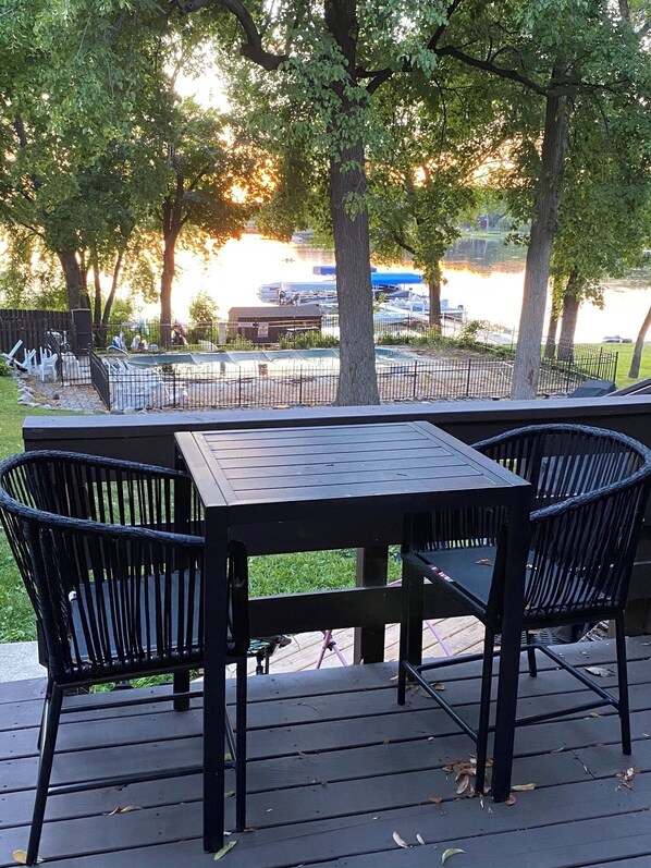 An outdoor deck with a table and chairs, overlooking a body of water with boats and a dock.