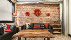 A living room with a brick wall, a wooden coffee table, a black leather sofa, and a red lamp. - Brand New ★ Prime Location ★ Exposed Brick Beauty! (Pittsburgh)