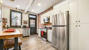 A modern kitchen with stainless steel appliances, a wooden dining table, and a brick accent wall. - Brand New ★ Prime Location ★ Exposed Brick Beauty! (Pittsburgh)