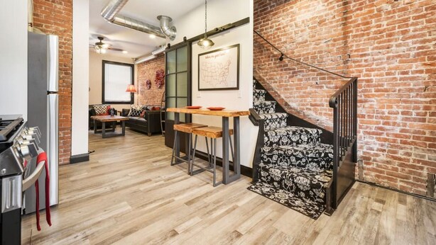 A modern kitchen with a brick wall, wooden flooring, and a dining area with a table and chairs. - Brand New ★ Prime Location  ★ Exposed Brick Beauty! (Pittsburgh)
