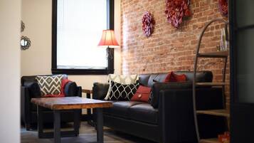 Ein Wohnzimmer mit Ziegelwand, einer schwarzen Ledersofa, einem Holztisch und einer roten Lampe.