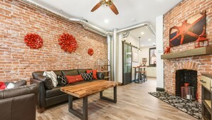 A modern living room with a brick wall, leather sofa, wooden coffee table, and a fireplace. - Brand New ★ Prime Location ★ Exposed Brick Beauty! (Pittsburgh)