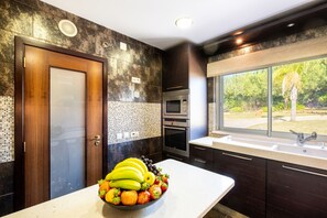 Une cuisine moderne dotée d’une grande fenêtre, d’un panier de fruits posé sur le plan de travail et d’un four encastré.