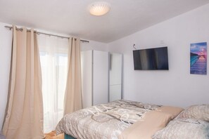 A bedroom with a bed, curtains, a TV, and a painting on the wall.