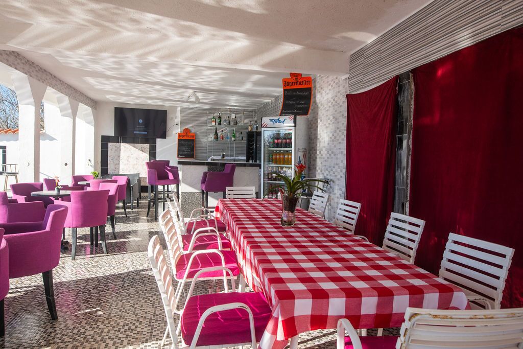 A restaurant with a checkered tablecloth, pink chairs, and a red curtain.