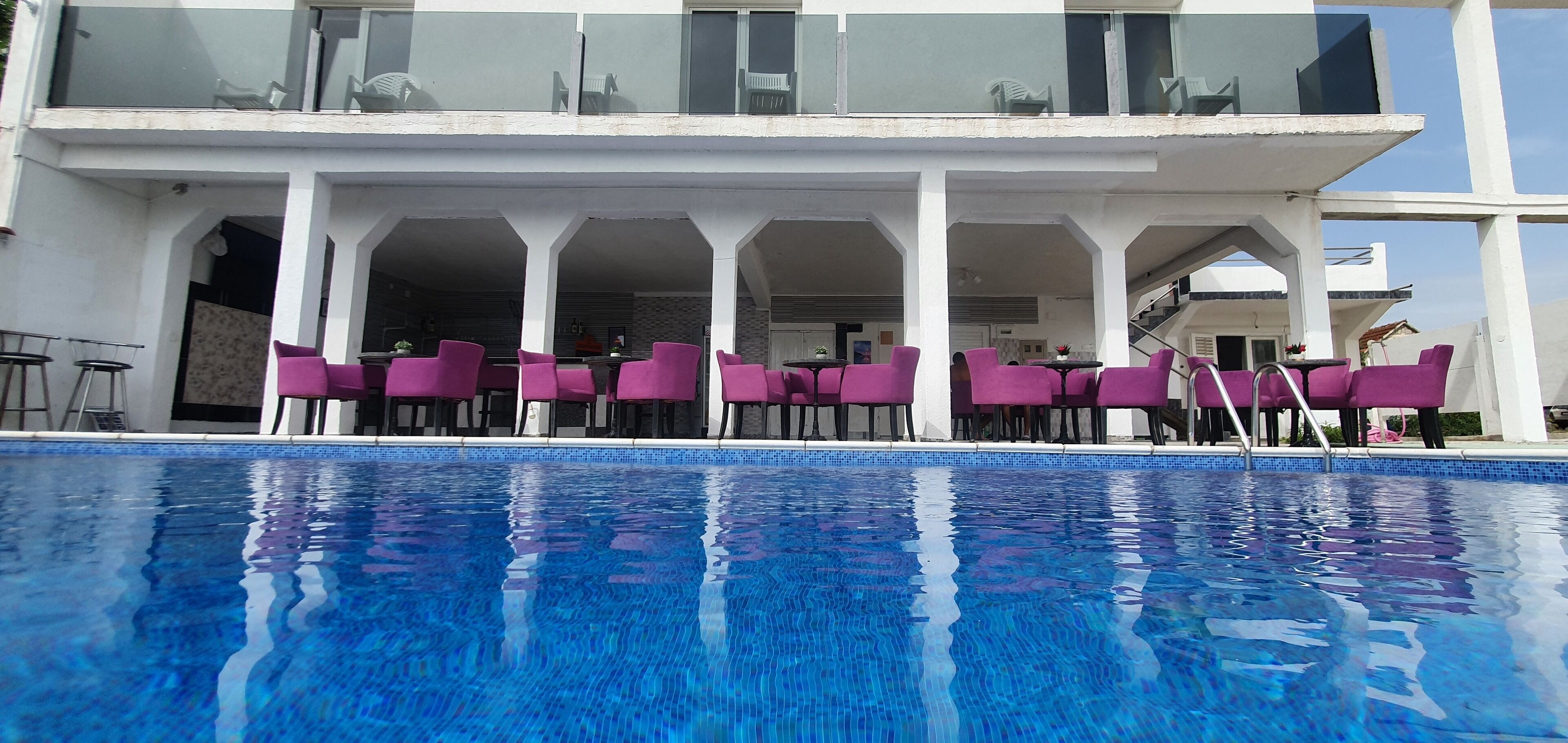 A poolside area with a clear blue pool, white pillars, and purple chairs.
