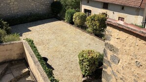 Un patio con escalones de piedra que conducen a un techo de tejas, rodeado de muros de piedra y follaje.