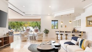 Un salon moderne avec un canapé, une table basse et des fauteuils. Une grande fenêtre offre une vue sur les arbres et donne sur un espace patio.