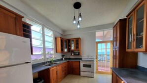 Eine Küche mit Holzausstattung, einem Kühlschrank, einem Backofen und einem Spülbecken. Ein Fenster lässt natürliches Licht herein und bietet einen Ausblick nach draußen.