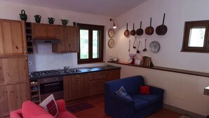 Un espacio habitable compacto con kitchenette, un sofá rojo, un sillón azul y una pequeña mesa de comedor.
