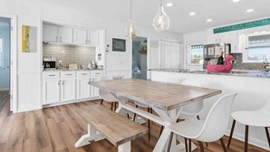 A modern kitchen with white cabinets, a wooden dining table, and pendant lights. - 4 Bedroom Cottage with amazing canal views (Ocean Isle Beach)