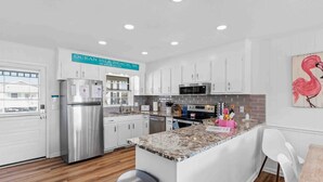A modern kitchen with white cabinets, stainless steel appliances, a granite countertop, and a wooden floor. - 4 Bedroom Cottage with amazing canal views (Ocean Isle Beach)