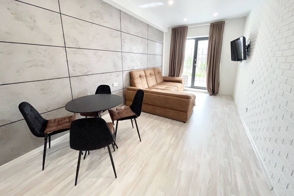 A modern living room with a sofa, a dining table with chairs, and a TV mounted on the wall.