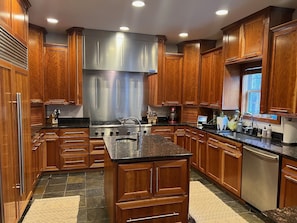 A modern kitchen with wooden cabinets, stainless steel appliances, and a granite countertop. - Custom home for entertainment for Masters week (Evans)