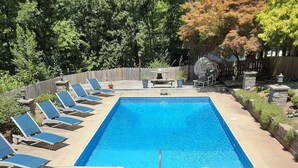 Una piscina rectangular con cubierta de madera, rodeada de sillas de descanso y plantas en macetas.