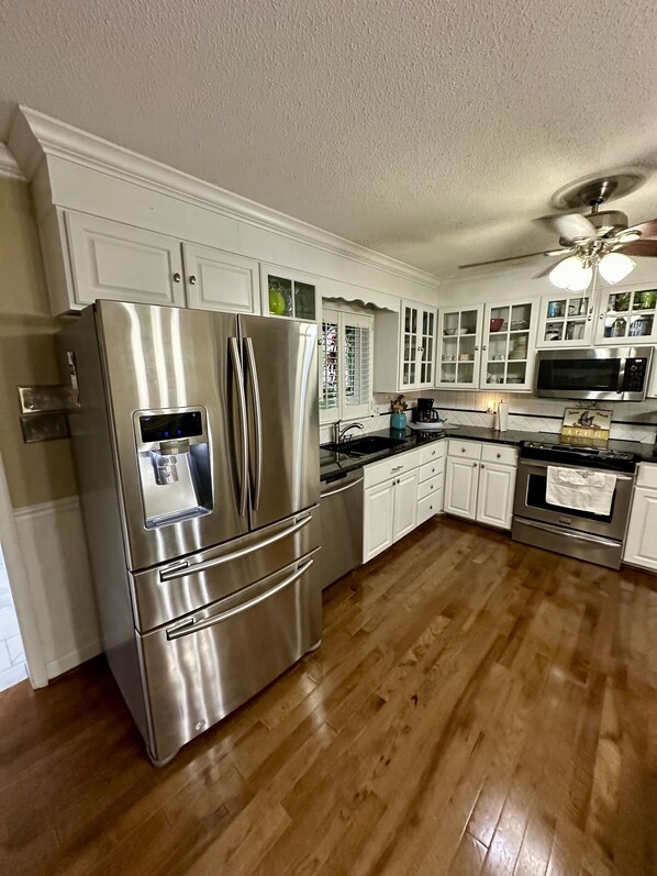 A modern kitchen with stainless steel appliances, white cabinetry, and a wooden floor.