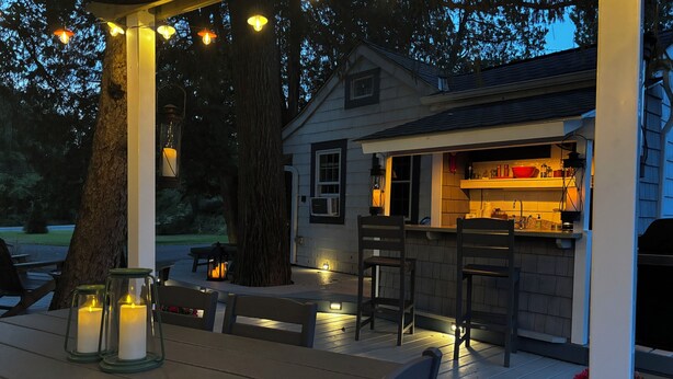 Une terrasse en bois avec des sièges extérieurs, un petit coin bar et des guirlandes lumineuses.