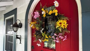 Une porte rouge ornée d’une composition florale décorative et dotée d’un heurtoir en métal noir.