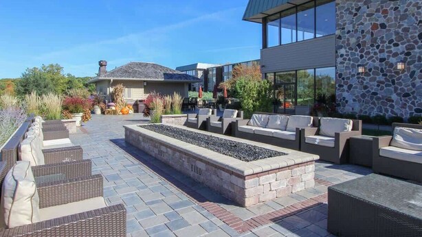 An outdoor patio area with wicker furniture, a stone fire feature, and a stone wall. - Lake Geneva Condo with Pool, Fireplace & Parking (Lake Geneva)