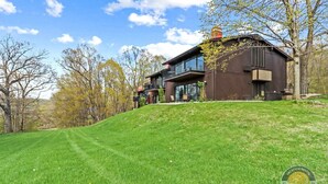 A modern two-story house with large windows and a balcony, surrounded by a well-maintained lawn and trees. - Lake Geneva Condo with Pool, Fireplace & Parking (Lake Geneva)