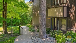 A building with a pathway leading to a door, surrounded by trees and plants. - Lake Geneva Condo with Pool, Fireplace & Parking (Lake Geneva)