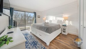 A bedroom with a bed, bedside tables, a desk, and a large window. - Lake Geneva Condo with Pool, Fireplace & Parking (Lake Geneva)