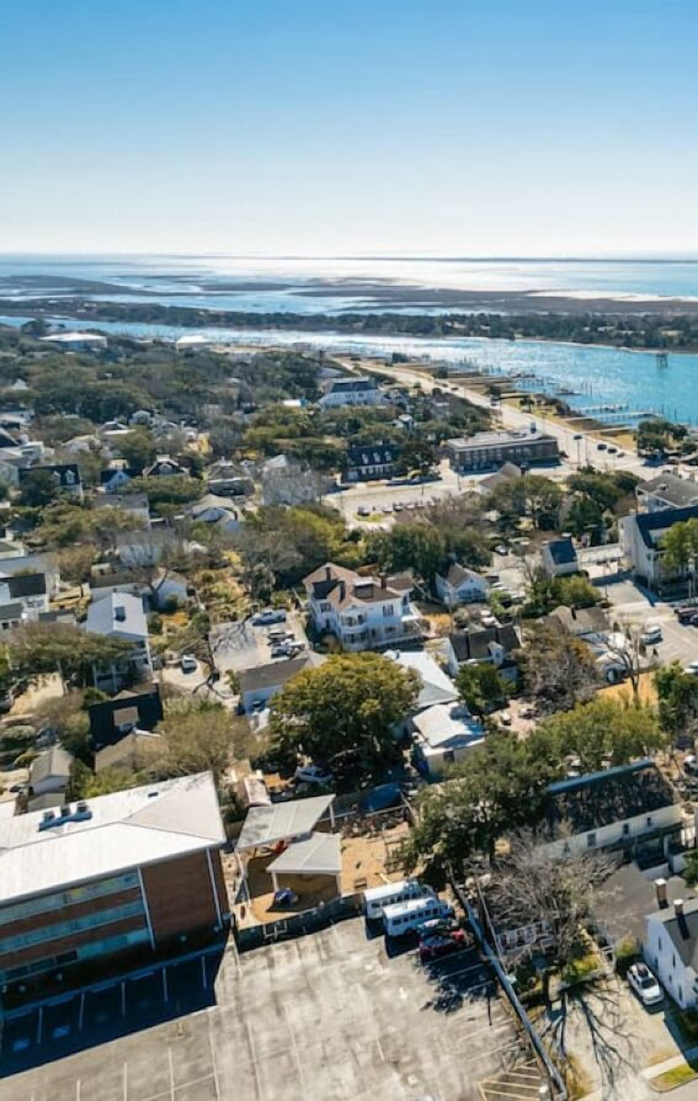 An aerial view of a coastal residential area with houses, a parking lot, and a marina.