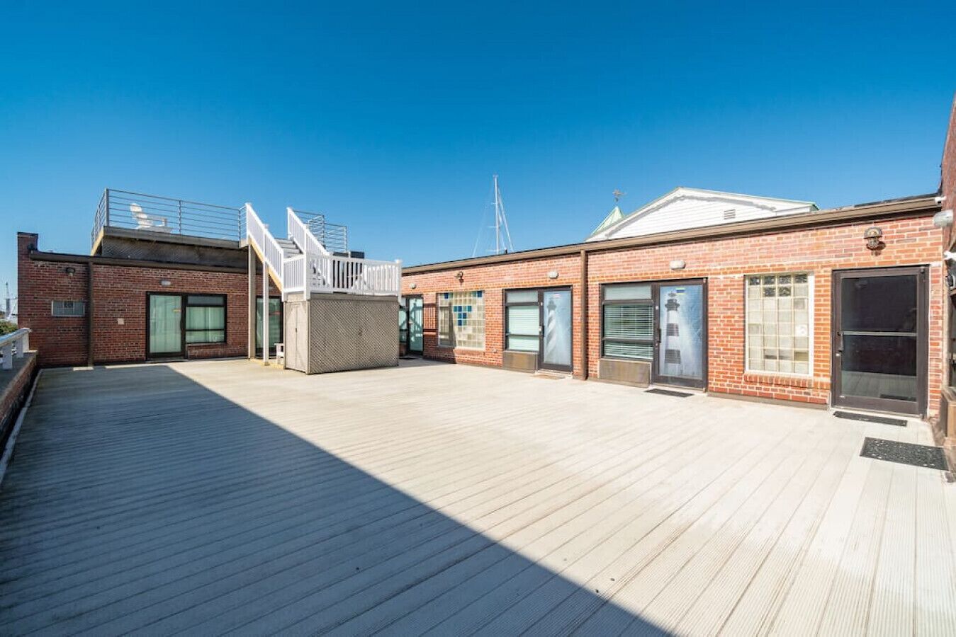 A rooftop deck with a wooden floor, a brick building with large windows, and a metal staircase.
