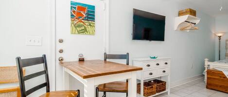 A dining area with a wooden table and chairs, a white cabinet with baskets, and a television mounted on the wall.