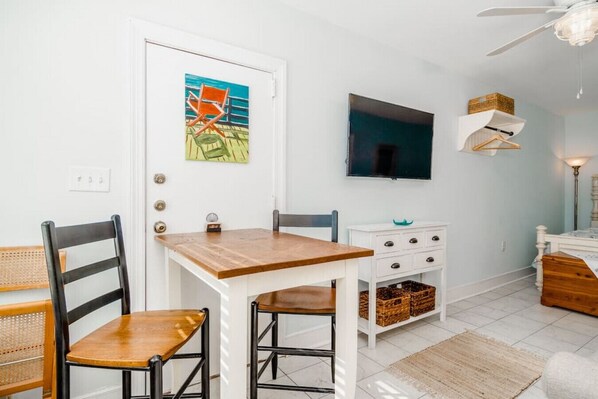 A dining area with a wooden table and chairs, a white cabinet with baskets, and a television mounted on the wall.